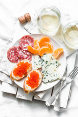 Delicious appetizer - red caviar sandwiches, blue cheese, salami, tangerines and white wine on a light background, top view. Flat lay