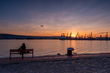 Fototapeta premium Girl watches the sunset at the sea station with ships.