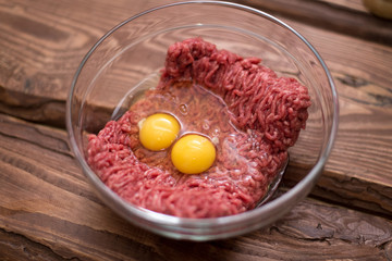 Fresh minced meat with chicken eggs on a plate on a wooden background for cooking.