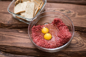 Fresh minced meat with chicken eggs on a plate on a wooden background for cooking.