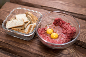 Cooking homemade meatballs - fresh raw minced meat and bread soaked in milk on a wooden background.