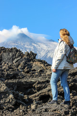 Naklejka premium A girl looking at Etna vulcan in clouds. Climbing to the Etna