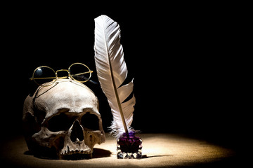 Drama or theater concept. Old inkstand with feather quill near skull with old retro glasses against...