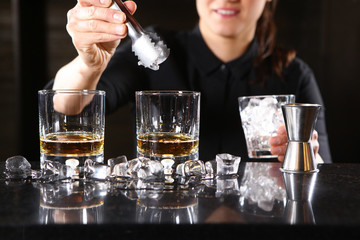 The bartender girl smiles and pours whiskey into glasses and adds ice. Photo on the bar in the restaurant. Girl out of focus.