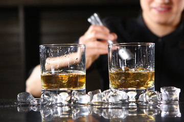 The bartender girl smiles and pours whiskey into glasses and adds ice. Photo on the bar in the restaurant. Girl out of focus.