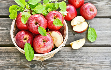 A lot of fresh Royal Red Gala apples with green leaf and water drop in basket on wooden background.