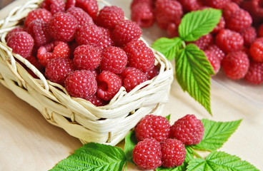 A lot of fresh Raspberry with green leaf in basket on wooden table.