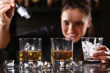 The bartender girl smiles and pours whiskey into glasses and adds ice. Photo on the bar in the restaurant. Girl out of focus.
