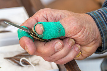 Obraz premium A craftsman is holding a small pocket knife in his right hand that he uses for carving. His thumb and fore-finger is covers in a green stretchy fabric that prevents objects from slipping