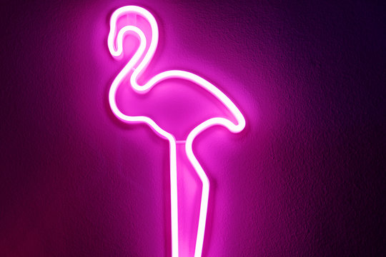 Pink flamingo neon light on the wall. Illuminated decorative figure of glowing flamingo shape sign decorating a wall.