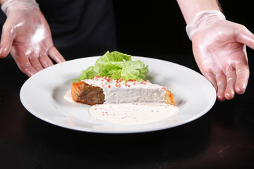 The hands of the chef serving dishes from a piece of salmon in a creamy caviar sauce on a white plate with salad leaves. Macro photo.