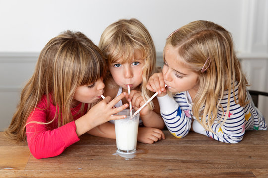 Three sisters blowing bubbles in a glass of milk with drinking straws