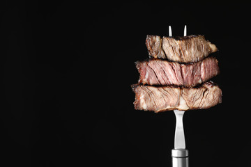 Fork with pieces of delicious barbecued meat on black background. Space for text © New Africa