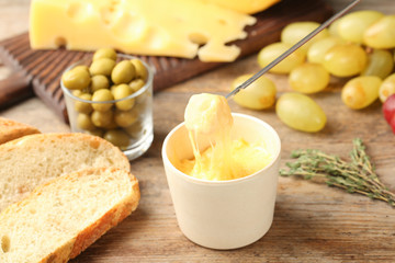 Piece of bread over bowl with delicious cheese fondue on wooden table