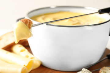Pot of delicious cheese fondue and fork with bread on table