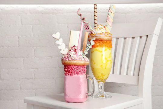 Tasty milk shakes with sweets in glassware on chair near brick wall