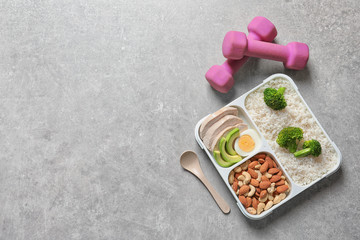 Container with natural healthy lunch, dumbbells and space for text on table, top view. High protein food