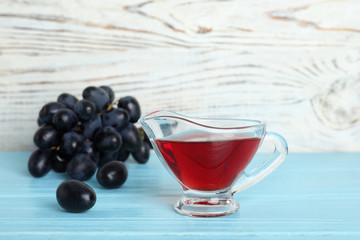 Glass gravy boat with wine vinegar and fresh grapes on wooden table