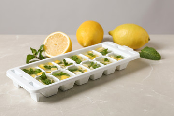 Ice cube tray with mint, lemon and water on grey table