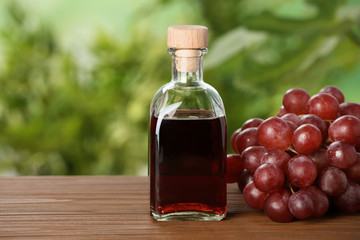 Bottle with wine vinegar and fresh grapes on wooden table against blurred background. Space for text