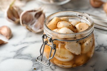Preserved garlic in glass jar on table, closeup. Space for text