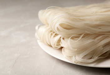 Plate with raw rice noodles on table, closeup. Space for text
