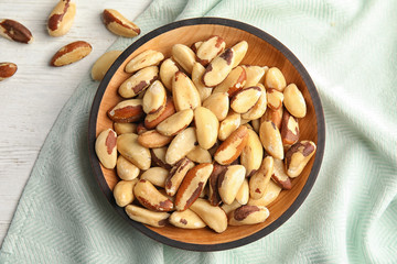 Plate with Brazil nuts and fabric on wooden table, top view