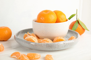 Plate and bowl with ripe tangerines on table