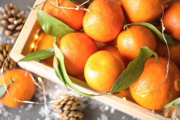 Wooden crate with ripe tangerines and Christmas lights, closeup