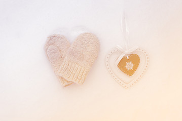 Knitted mittens and a wooden heart on snow
