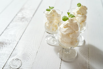 Glasses with a dessert of whipped cream with a fresh mint leaf on a white wooden table.