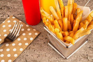 French fries basket with ketchup, napkin and fork on concrete background. Close up.