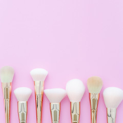 Flat lay. Set of fashionable gold makeup brushes on pink background with copy space.