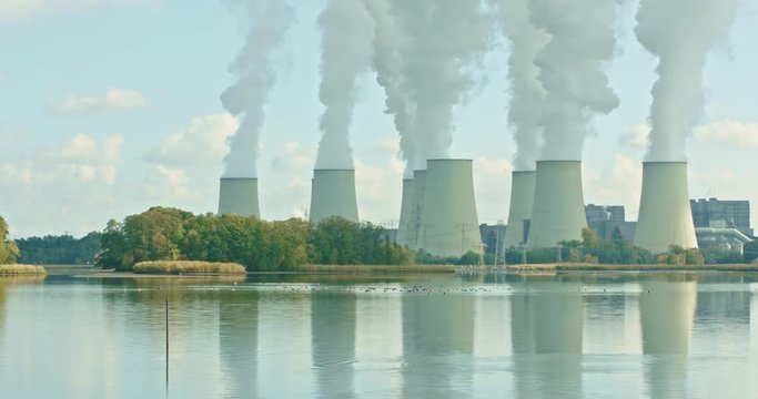 Lignite-fired power station in front of a lake, a flock of birds starts, the steam reflects in the water, an idylic picture of industry and nature