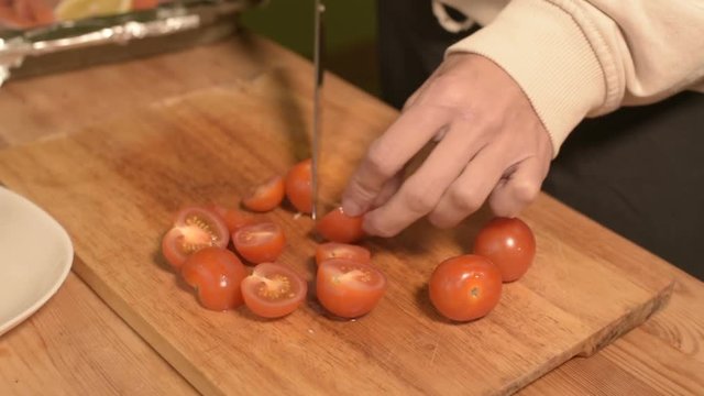 Closeup of the hands of a girl at the home kitchen on a wooden cutting board small cherry tomatoes. Home cooking