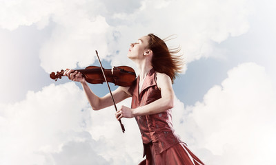 Woman violinist in red dress playing melody against cloudy sky © adam121