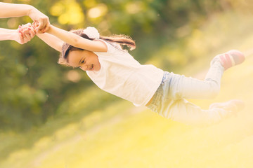 Mother turns little daughter in circle holding her hands on sunny grassy lawn in park