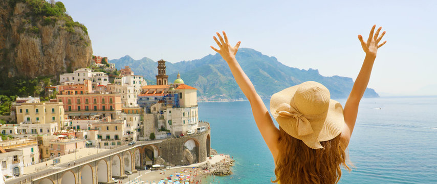 Summer Holiday In Italy. Panoramic Back View Of Young Woman With Straw Hat With Raised Arms Looking At Atrani Village, Amalfi Coast, Italy.