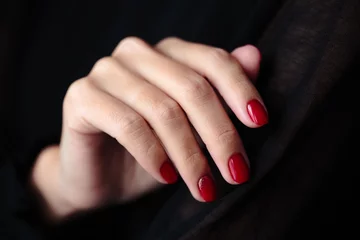 Gorgeous manicure, clssic red color nail polish, closeup photo. Female hands over dark fur background