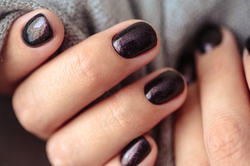 Gorgeous manicure, dark purple tender color nail polish, closeup photo. Female hands over simple background of casual clothes