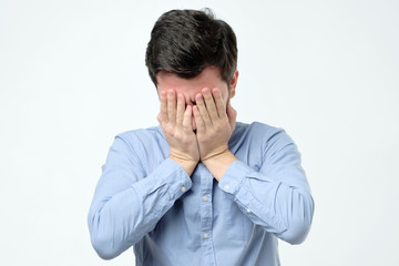 Man covering face with hand while standing against grey background