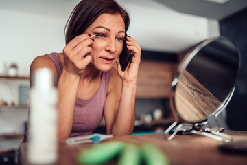 Women doing makeup eyebrow and talking on smart phone