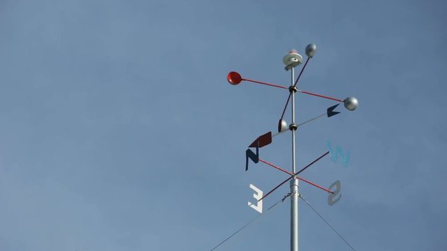 Weather vane rotates in the wind against cloudy sky.