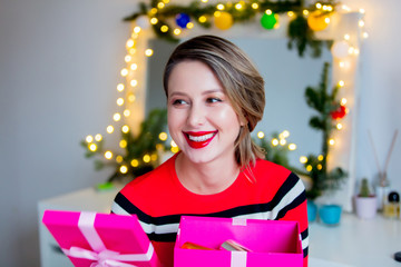 Beautiful woman in red sweater holding a gift box. Makeup mirror on background