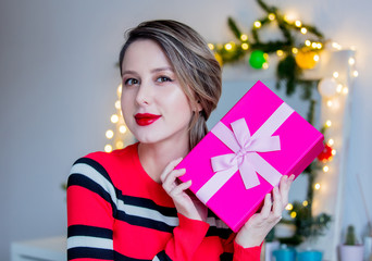 Beautiful woman in red sweater holding a gift box. Makeup mirror on background