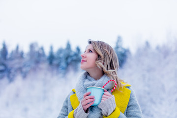 Beautiful girl in gray coat with cup of hot drink in a snow forest. Christmas of Valentine Day season time