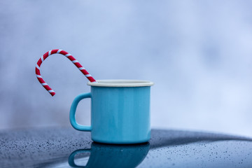 Obraz na płótnie Canvas Blue cup of coffee with hot drink and candy inside on car roof with snow trees on background