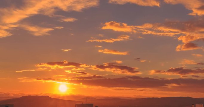 timelapse of sunset scene with sun fall behind the clouds and mountains in background, time lapse shot, warm colorful sky with soft clouds