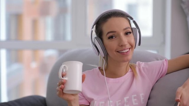 Smiling woman relaxing at home sofa with cup of tea and good music