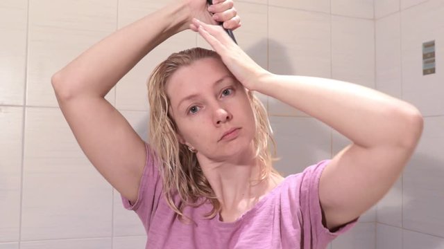 Middle aged blond woman brushing her wet hair with a hair brusher in bathroom